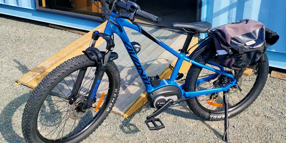 Extra extra small blue Avanti e-bike with pannier bag parked outside Nelson Cycle Hire
