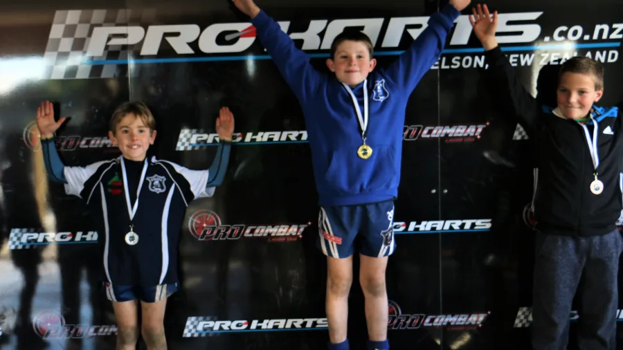 Three young racers standing on the Pro Karts podium in Nelson with medals and raised arms