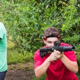 Two players aiming laser tag rifles while hiding in outdoor bush at Pro Combat Laser Tag in Nelson