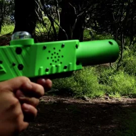 First-person view aiming a green laser tag gun in a forested area at Pro Combat Laser Tag in Nelson