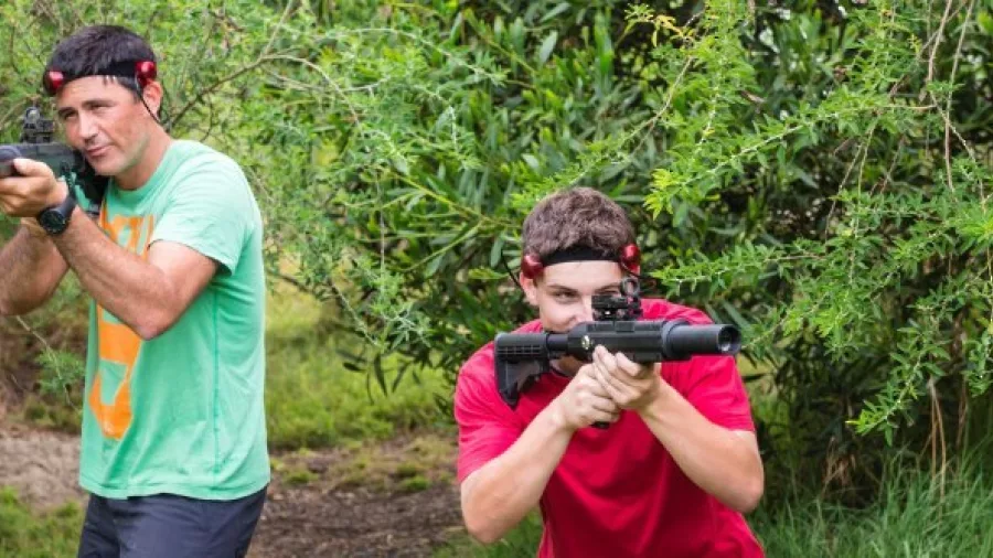 Two players aiming laser tag rifles while hiding in outdoor bush at Pro Combat Laser Tag in Nelson
