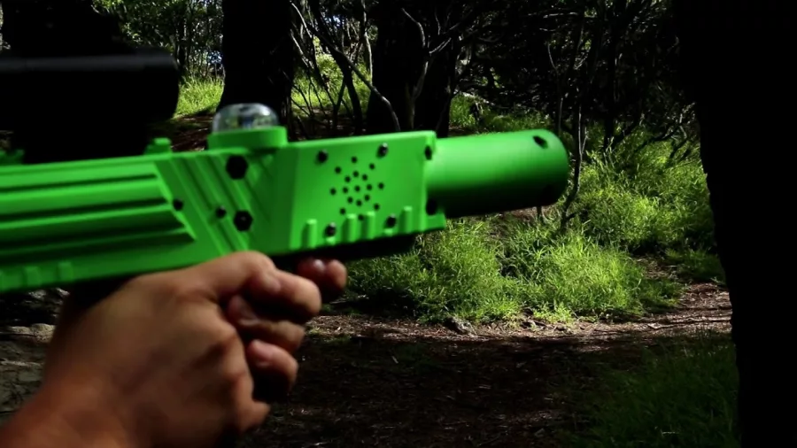 First-person view aiming a green laser tag gun in a forested area at Pro Combat Laser Tag in Nelson
