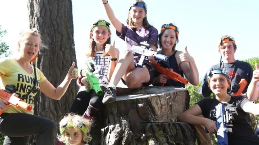 Group of adults and kids smiling with laser tag guns during an outdoor Pro Combat Laser Tag session in Nelson