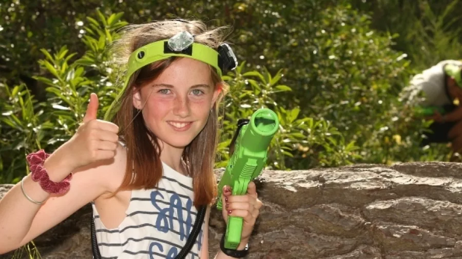 Young girl giving a thumbs up while holding a green laser tag gun during an outdoor game at Pro Combat in Nelson