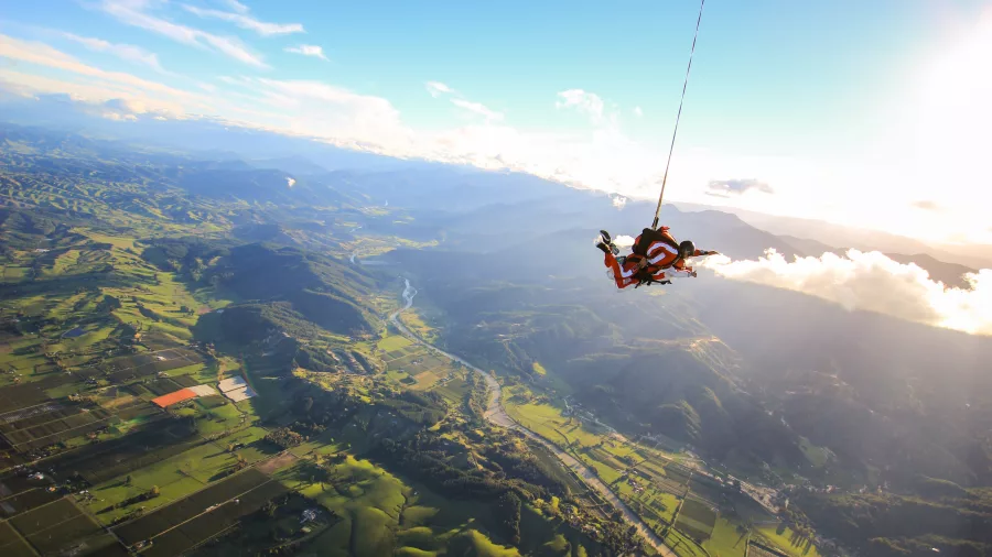 Tandem skydivers descend over the scenic Tasman Hills with expansive farmland and valleys below