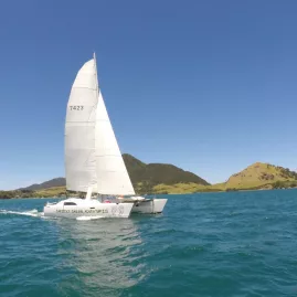 Catamaran sailing in clear blue waters near green headlands in the Bay of Islands