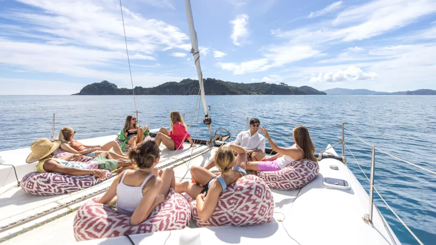 Travellers lounging on beanbags aboard a sailing catamaran in the Bay of Islands near Paihia