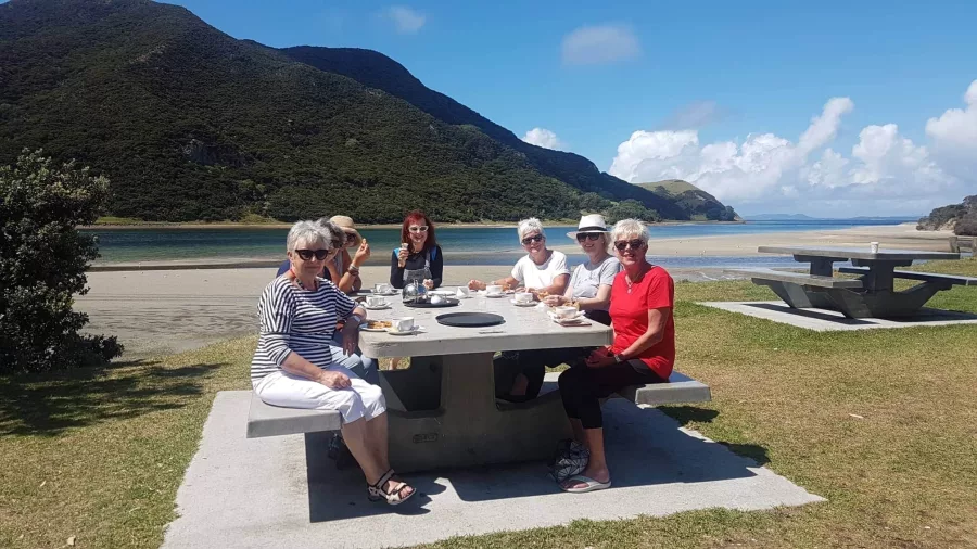 Group enjoying lunch at a picnic table by the beach during a Cape Reinga tour