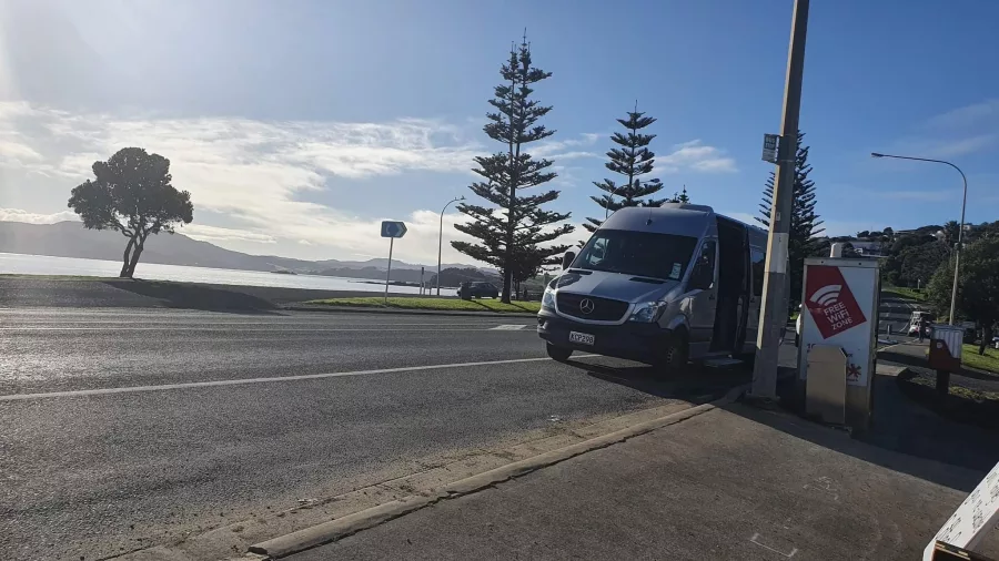 Silver tour van parked along Cable Bay road with coastal view in Northland