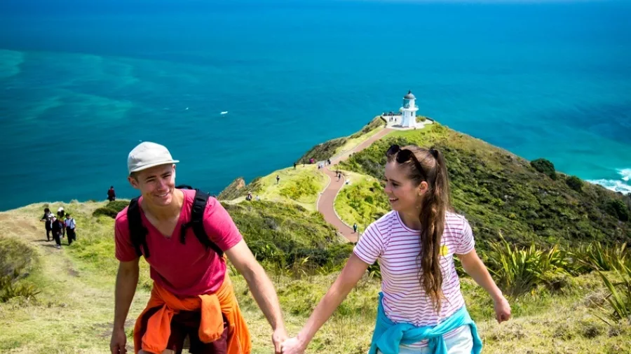 Couple holding hands on the Cape Reinga track with lighthouse and ocean in background