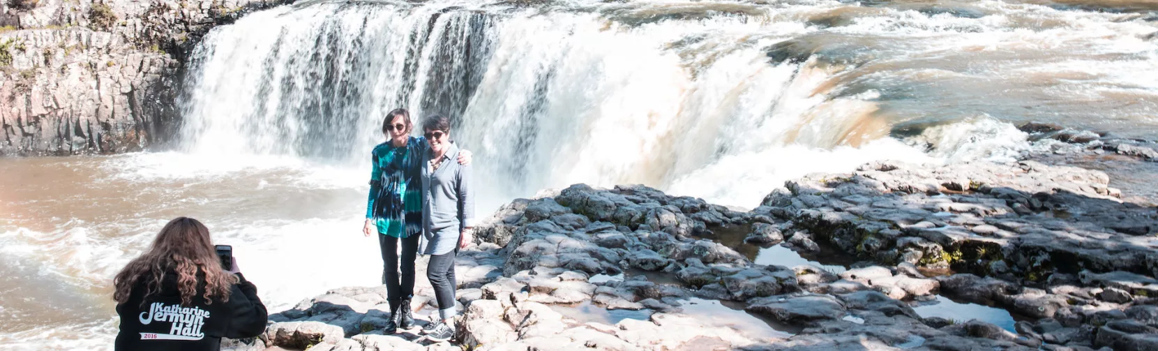 Two people posing for a photo in front of Haruru Falls during a Bay of Islands tour
