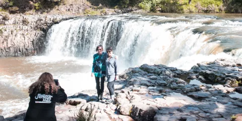 Two people posing for a photo in front of Haruru Falls during a Bay of Islands tour