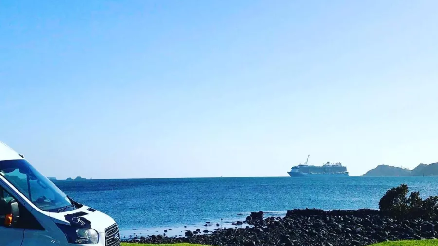 Bay of Islands Tours van parked on the coast with a cruise ship in the distance
