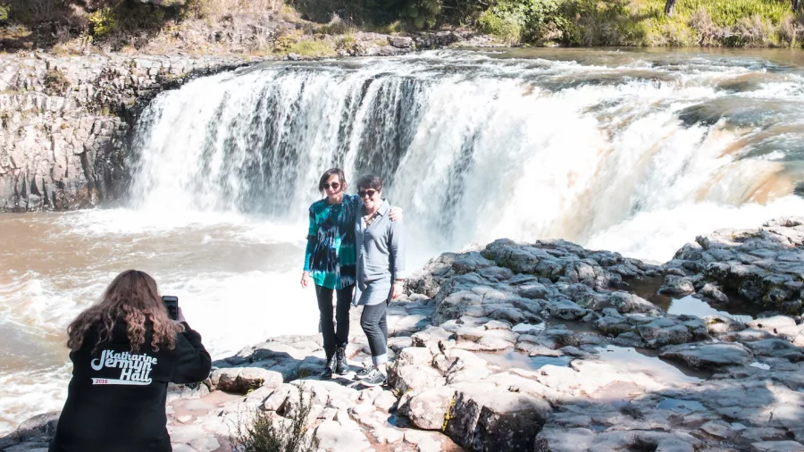 Two people posing for a photo in front of Haruru Falls during a Bay of Islands tour