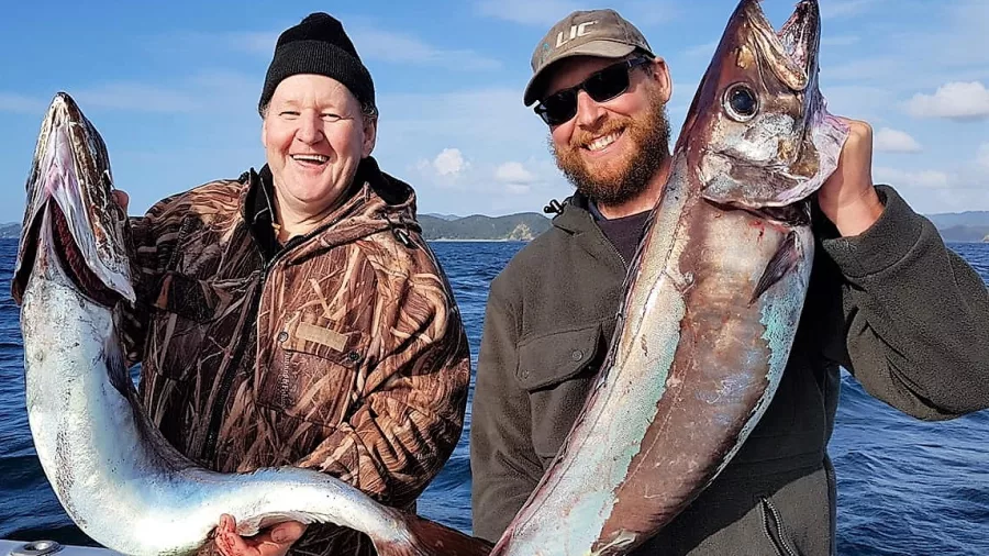 Two smiling anglers holding freshly caught gemfish on a boat in New Zealand