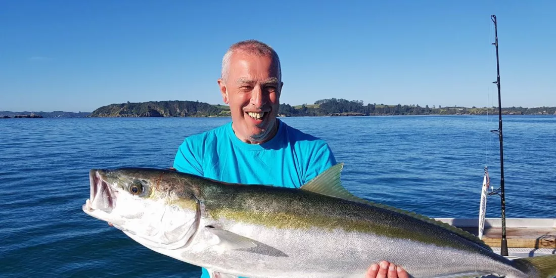 Smiling man on a boat holding a large kingfish with calm sea and island in the background