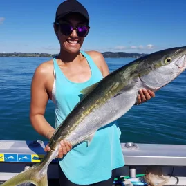 Woman smiling on a boat while holding a large kingfish under a clear blue sky
