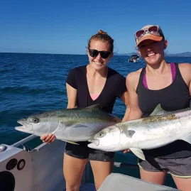 Two women on a boat smiling and holding freshly caught kingfish in the Bay of Islands