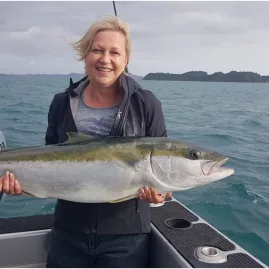 Woman smiling and holding a freshly caught kingfish on a fishing boat in the Bay of Islands