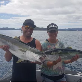Smiling couple holding two kingfish with the fish locking jaws on a boat in the Bay of Islands