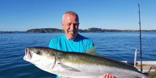 Smiling man on a boat holding a large kingfish with calm sea and island in the background