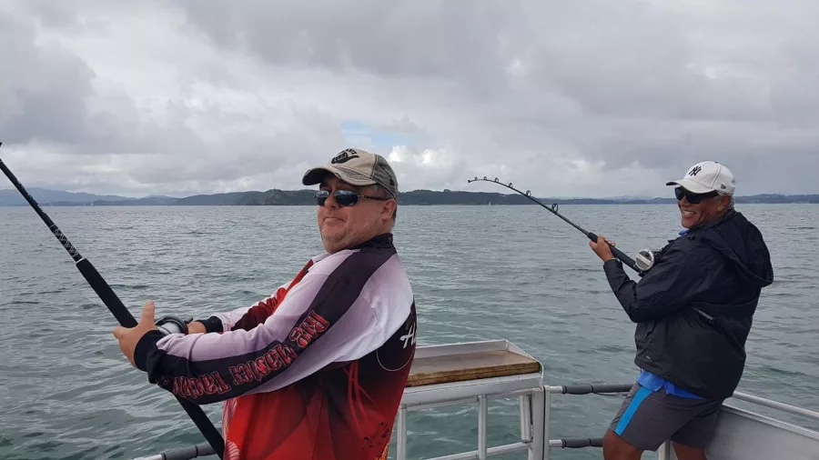 Two men smiling and holding bent fishing rods during an active moment on a private fishing charter