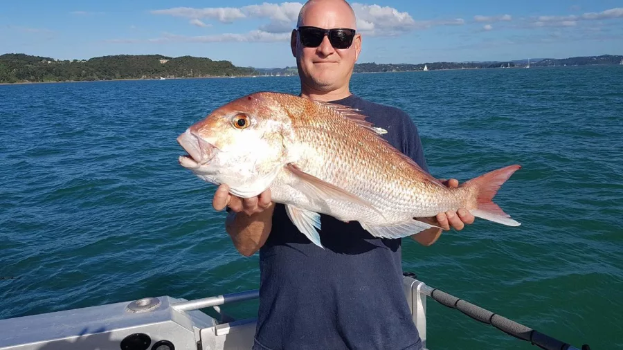 Man holding a large kingfish on a boat with ocean and islands in the background