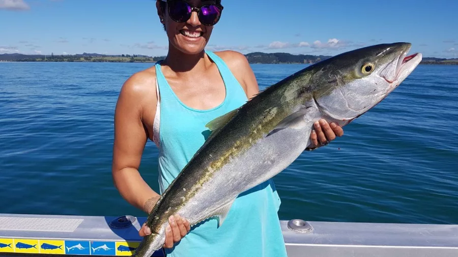 Woman smiling and holding a freshly caught kingfish on a private fishing charter in the Bay of Islands