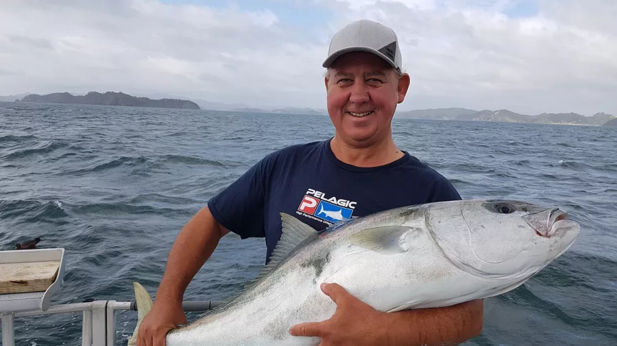 Man holding a large kingfish on a boat with ocean and islands in the background