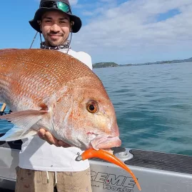 Angler holding a large snapper caught using a 7-inch orange soft bait in the Bay of Islands