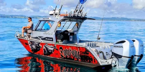 Fishing charter boat with custom red and black wrap floating on calm water in the Bay of Islands