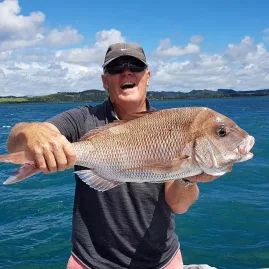 Older man smiling and holding a medium-large snapper on a sunny day in the Bay of Islands