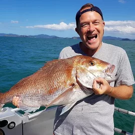 Man laughing while holding a large snapper on a fishing boat in the Bay of Islands