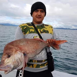 Man in a beanie holding a large snapper fish on a boat in the Bay of Islands