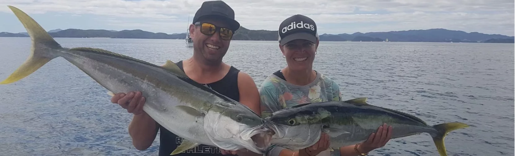 Man and woman smiling while holding two kingfish caught on a fishing trip in the Bay of Islands