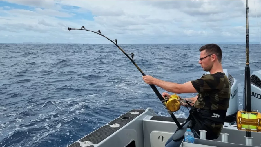 Man holding a fishing rod as he fights a marlin offshore in the Bay of Islands