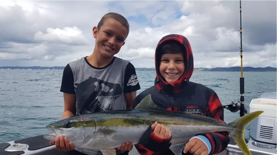 Two smiling kids holding a freshly caught kingfish during a fishing trip in the Bay of Islands