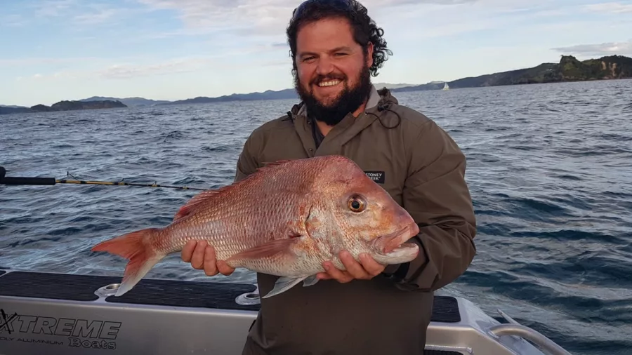 Man holding a freshly caught snapper during a fishing trip in the Bay of Islands