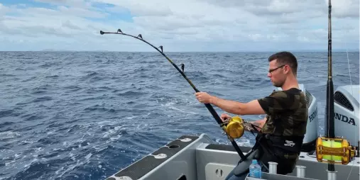 Man holding a fishing rod as he fights a marlin offshore in the Bay of Islands