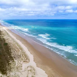 A stunning aerial view of 90 Mile Beach in New Zealand, showcasing its vast golden shoreline and turquoise ocean waves stretching into the horizon.