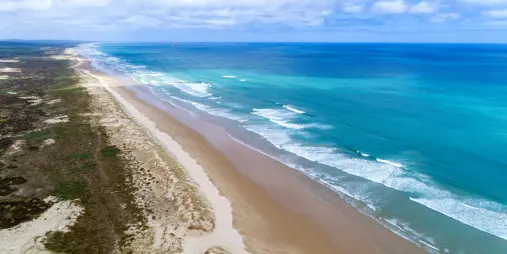 A stunning aerial view of 90 Mile Beach in New Zealand, showcasing its vast golden shoreline and turquoise ocean waves stretching into the horizon.