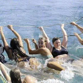 A group of excited travellers enjoying boomnetting in the Bay of Islands, New Zealand, splashing in the ocean while holding onto a submerged net.