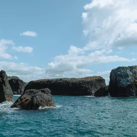 Dramatic volcanic rock formations rising from the turquoise waters of the Bay of Islands, set against a partly cloudy sky.