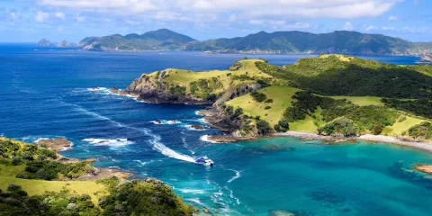 A breathtaking aerial view of the Bay of Islands, showcasing turquoise waters, rugged coastline, and lush green hills under a bright blue sky.