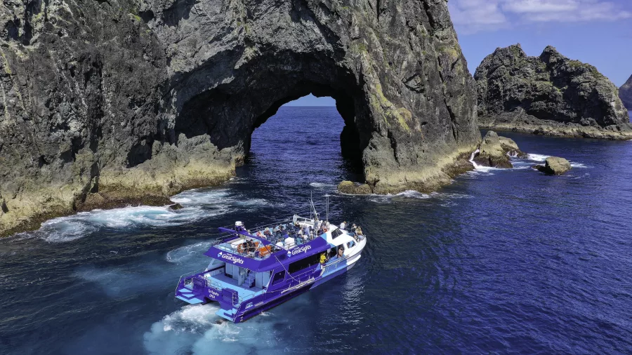 Te Papahu tour boat navigating the iconic Hole in the Rock at Piercy Island in the Bay of Islands, New Zealand.