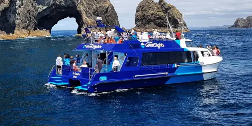 Scenic boat tour at the Bay of Islands, passing through the famous Hole in the Rock formation under a clear blue sky.