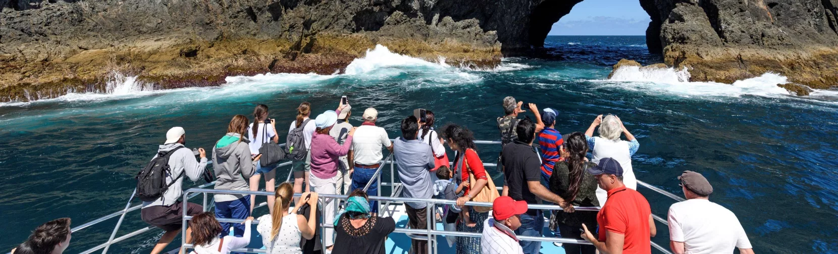 Tourists on a boat approaching the famous Hole in the Rock at Motukokako Island, Bay of Islands, New Zealand.