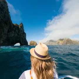 Woman on a boat tour approaching the famous Hole in the Rock at Motukokako Island, Bay of Islands, New Zealand.