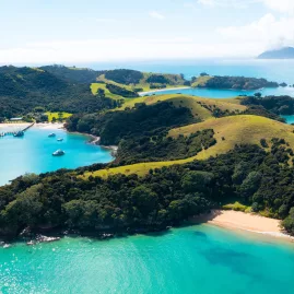 A breathtaking aerial view of Urupukapuka Island in the Bay of Islands, New Zealand, featuring lush green hills, sandy beaches, and turquoise waters.
