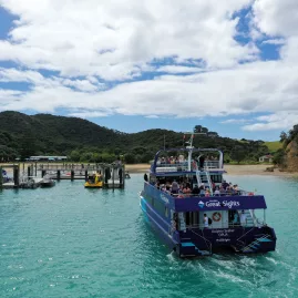 A cruise boat departing from Urupukapuka Island jetty in the Bay of Islands, New Zealand, with turquoise waters and scenic hills in the background.